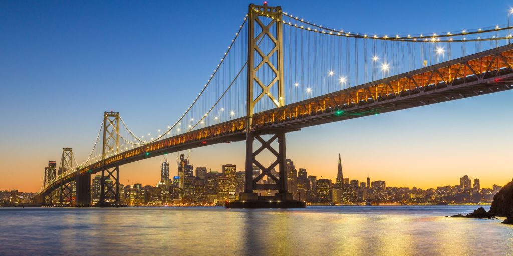 Classic panoramic view of famous Oakland Bay Bridge with the skyline of San Francisco in the background illuminated in beautiful twilight after sunset in summer, California, USA