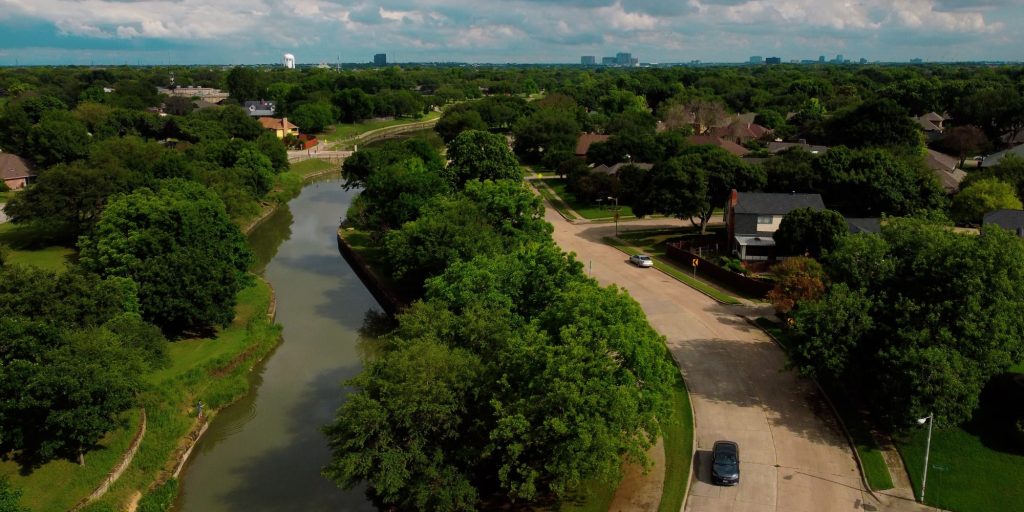 An aerial drone photo of a sunny summer day in Plano Texas next to a river park with a car driving on the street