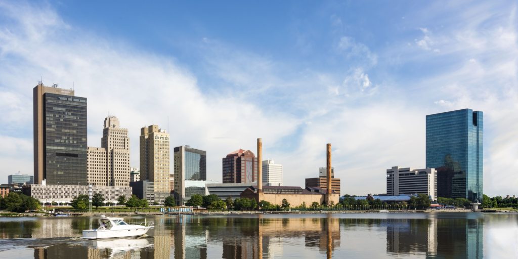 A panoramic view of downtown Toledo Ohio's skyline reflecting into the Maumee river with a power boat cruising by. A beautiful blue sky with white clouds for a backdrop.